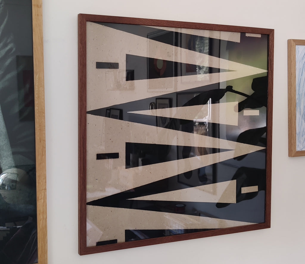 Abstract art piece with geometric shapes in a wooden frame on a wall.