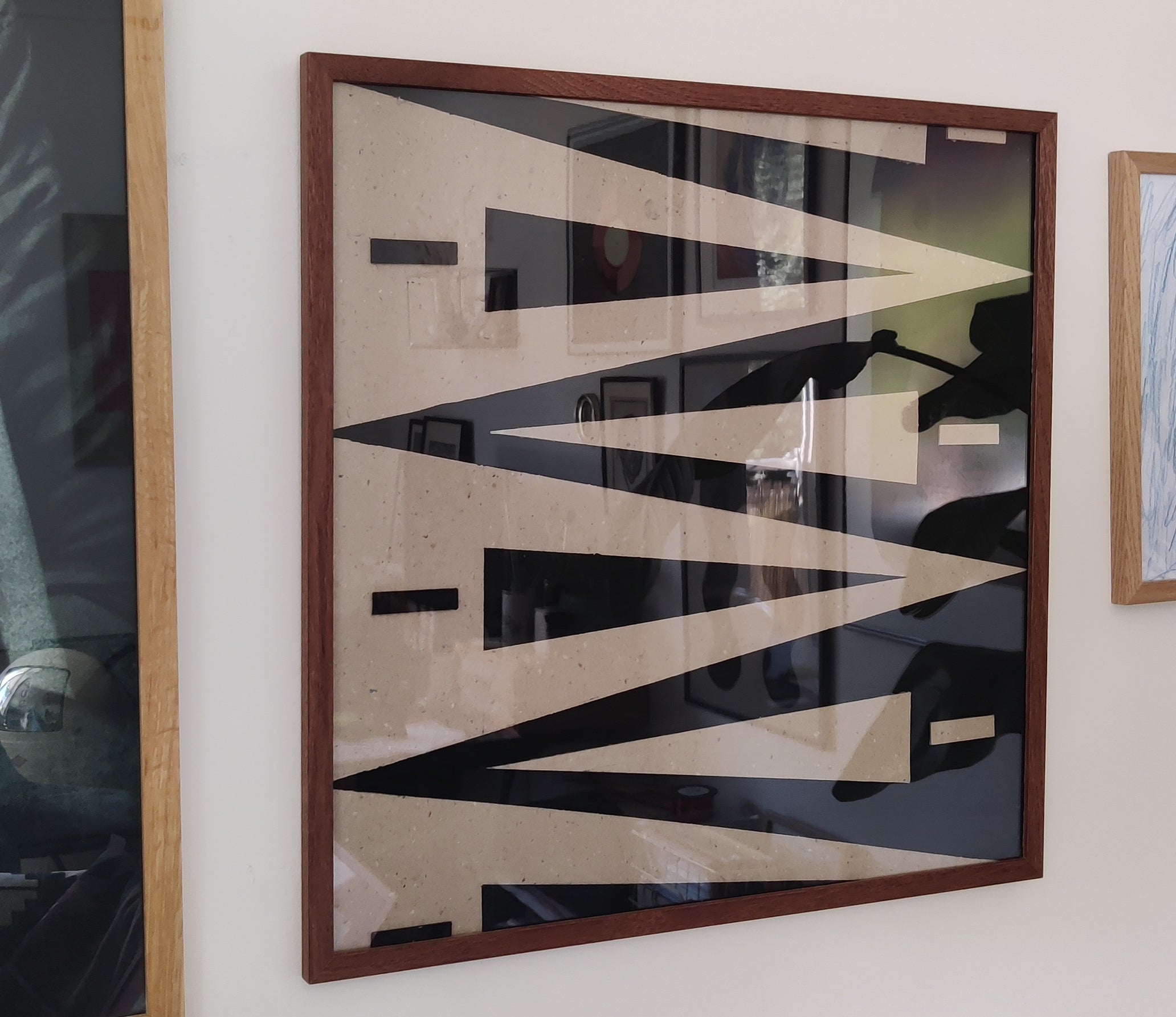 Abstract art piece with geometric shapes in a wooden frame on a wall.