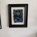 Framed paper pulp piece with blue and black pattern on a white wall