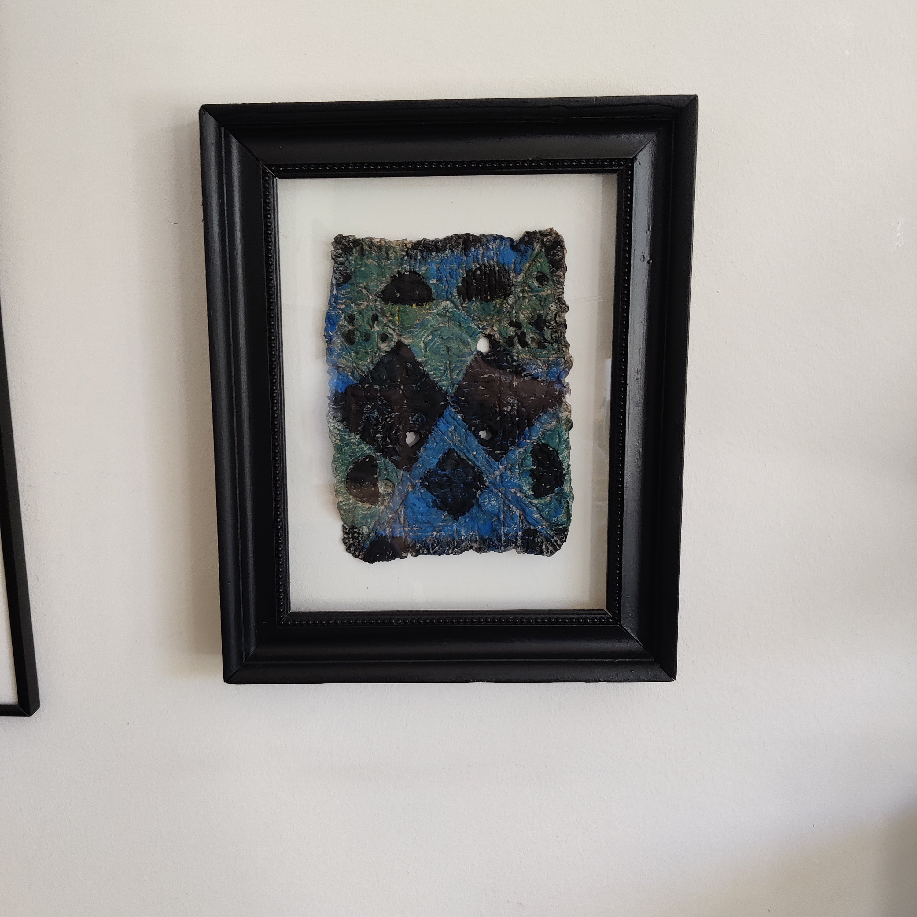 Framed paper pulp piece with blue and black pattern on a white wall