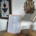 Framed artwork with abstract design on a wooden surface, with another piece of art and a lamp in the background.