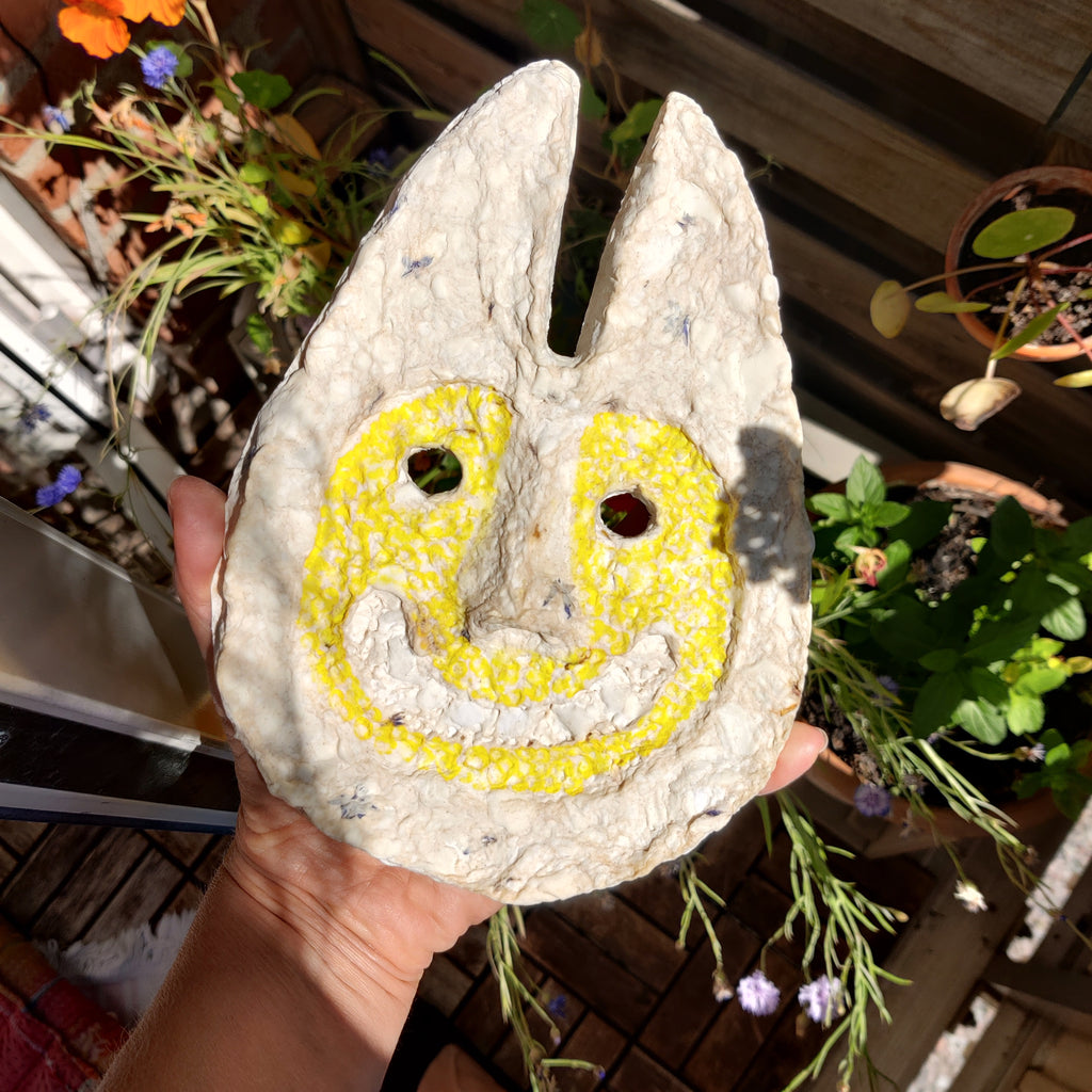 Decorative stone with a smiley face design held in front of plants